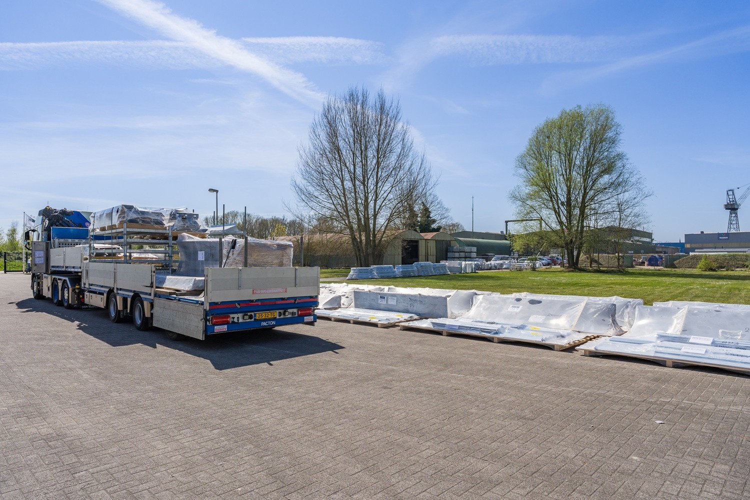 Vrachtwagen op het buitenterrein van VPT Versteeg, beladen met gevelonderdelen en materialen voor transport en montage op locatie, onder een heldere blauwe lucht.